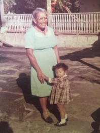 Una abuela sonriente le da la mano a su nieta pequeña en un lugar al aire libre.